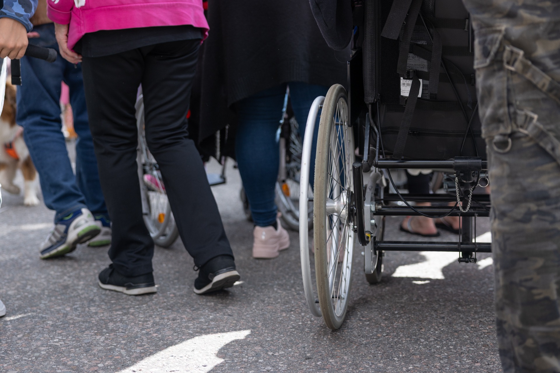 Ihmisiä liikkumassa ulkona, keskellä pyörätuolia käyttävä henkilö. Kuva havainnollistaa arjen liikkumisen ja esteettömyyden merkitystä.